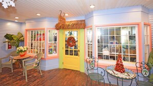 A cozy interior with a yellow door, a small Christmas tree, wicker chairs, and a table with a vase of flowers.