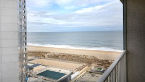 A view of a beach from a balcony, including a swimming pool and a parking area.