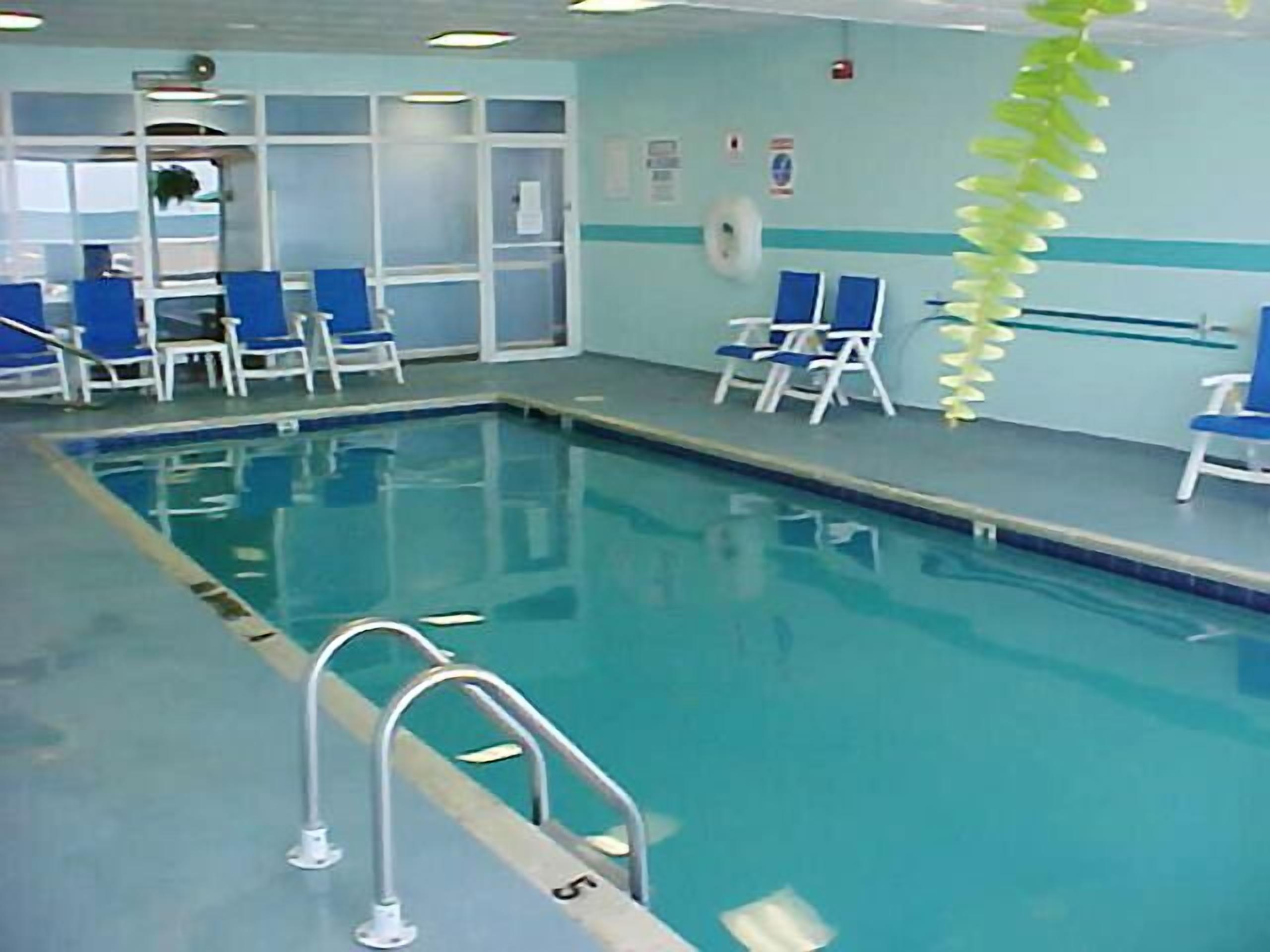 An indoor swimming pool with clear blue water, surrounded by blue chairs and a white wall with a green stripe.