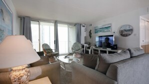 A modern living room with a sofa, armchair, and a coffee table. There is a television on a stand and a lamp on a side table.