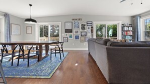 A spacious living room with a dining area, a gray sofa, wooden flooring, and a ceiling fan.