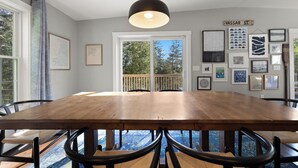 A dining area with a large wooden table, black chairs, and a hanging pendant light.
