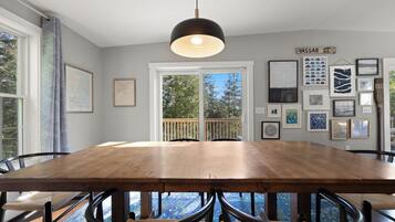 Un espace repas avec une grande table en bois, des chaises noires et un luminaire suspendu.