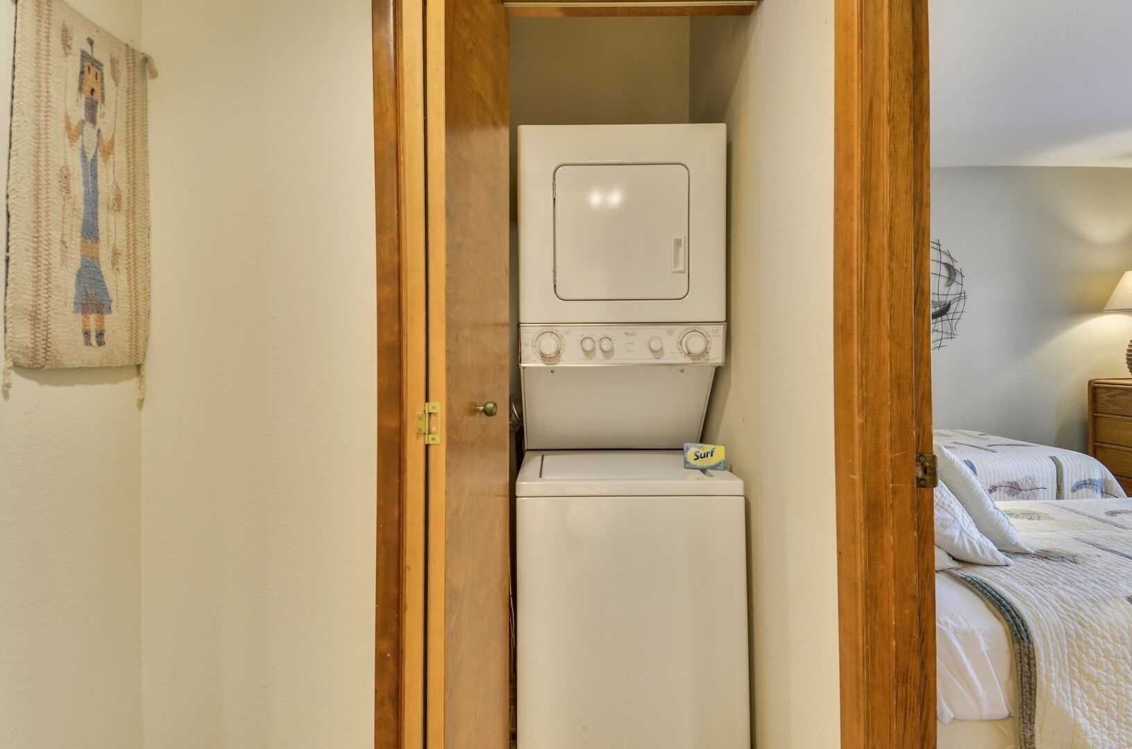 Un lavadero pequeño con lavadora y secadora, un marco de puerta de madera y una cama con edredón acolchado.