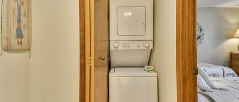 Un lavadero pequeño con lavadora y secadora, un marco de puerta de madera y una cama con edredón acolchado.