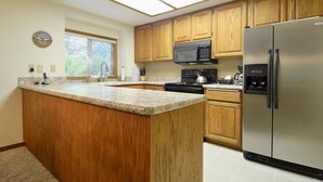 Cocina con gabinetes de madera, refrigerador de acero inoxidable, microondas y estufa.