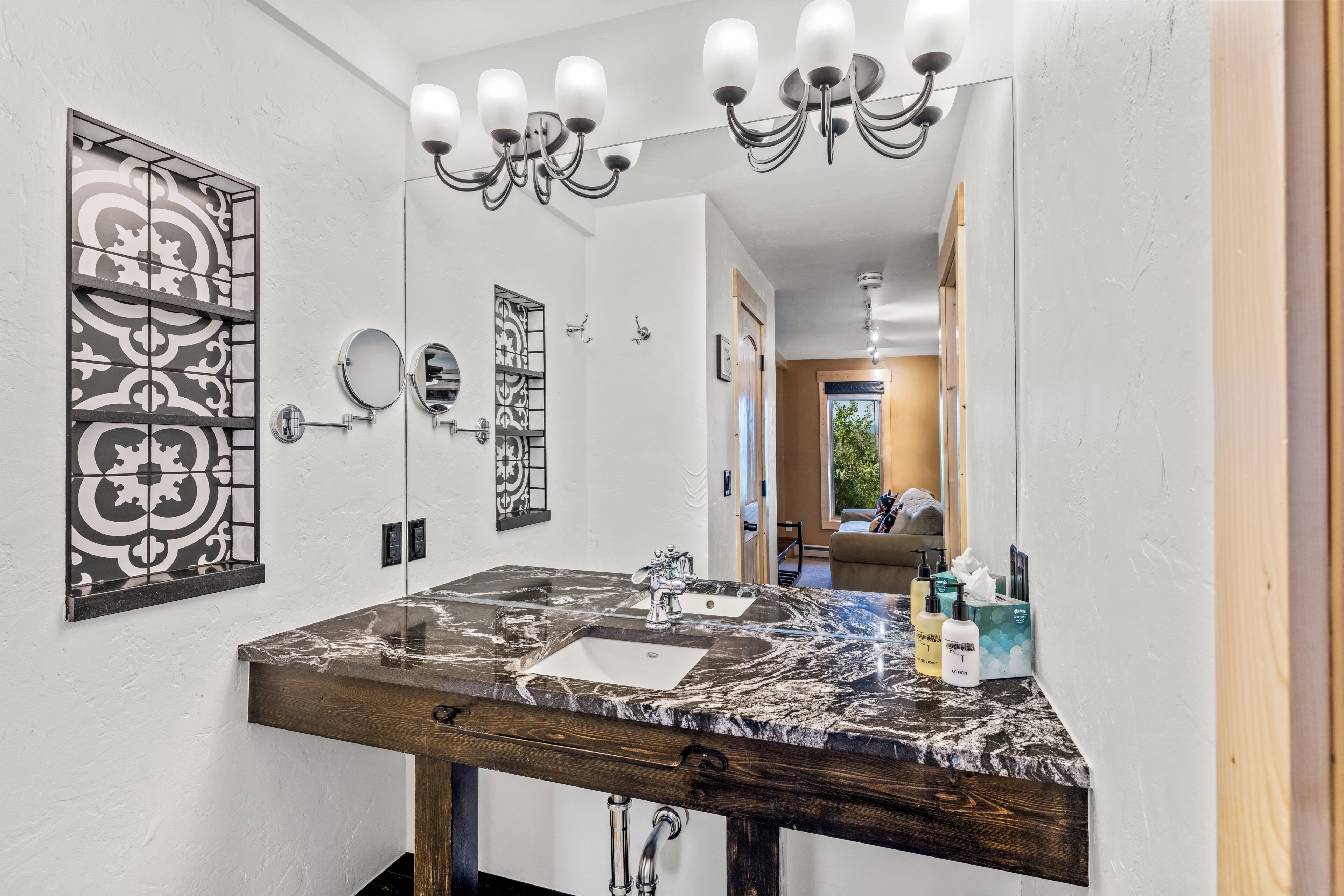 A bathroom with a marble sink, a wooden vanity, a chandelier, and decorative wall art.