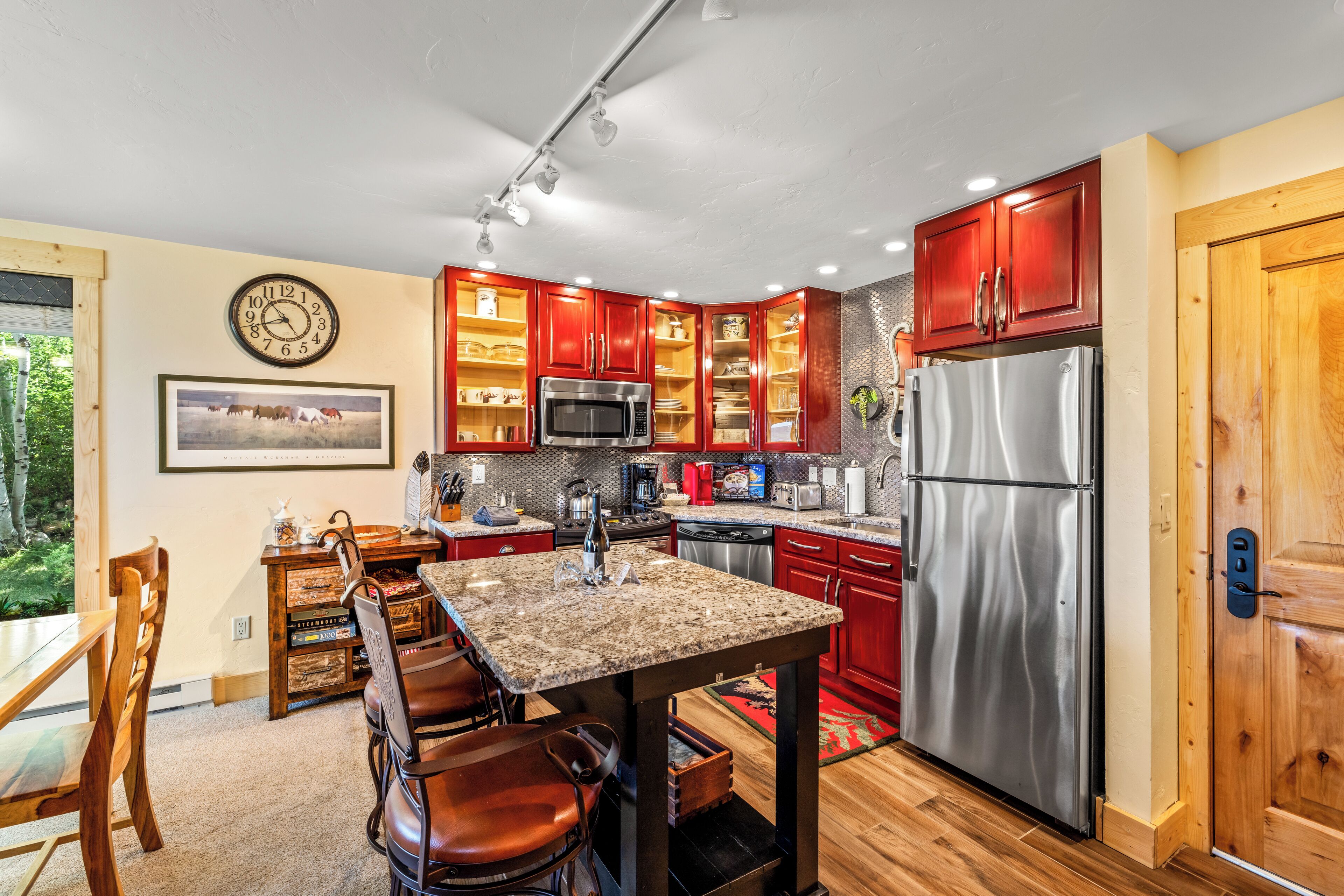 Una cocina con armarios rojos, electrodomésticos de acero inoxidable, una mesa de comedor de madera y un reloj en la pared.