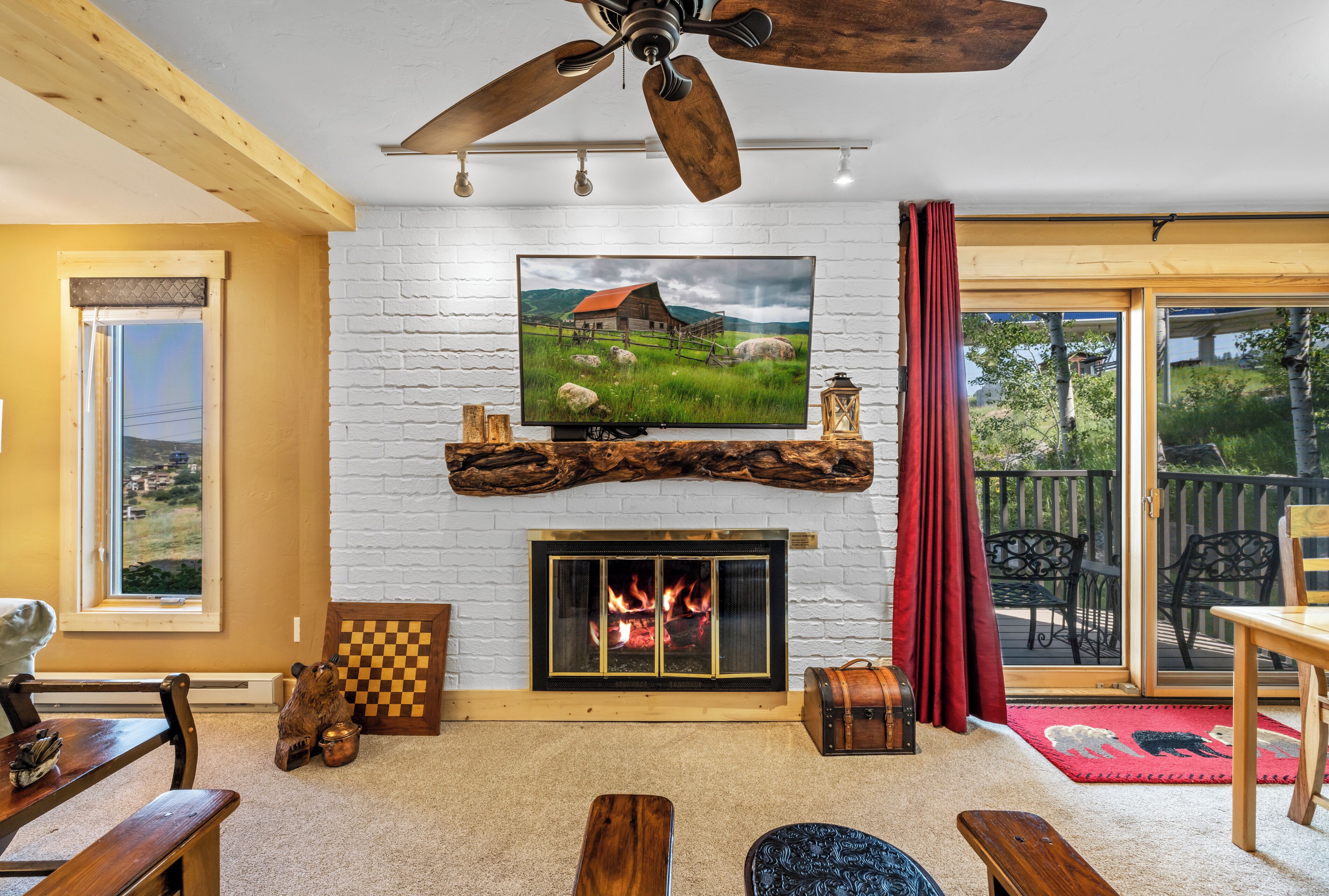 A cozy living room with a fireplace, a television mounted above it, and a ceiling fan.