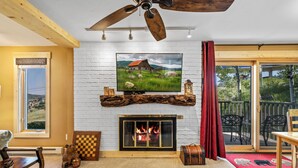 Un salon chaleureux avec une cheminée, un téléviseur fixé au-dessus et un ventilateur de plafond.