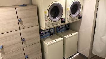 A laundry area with two front-loading washers and dryers, a wooden cabinet with numbered locks, and a clock on the wall.