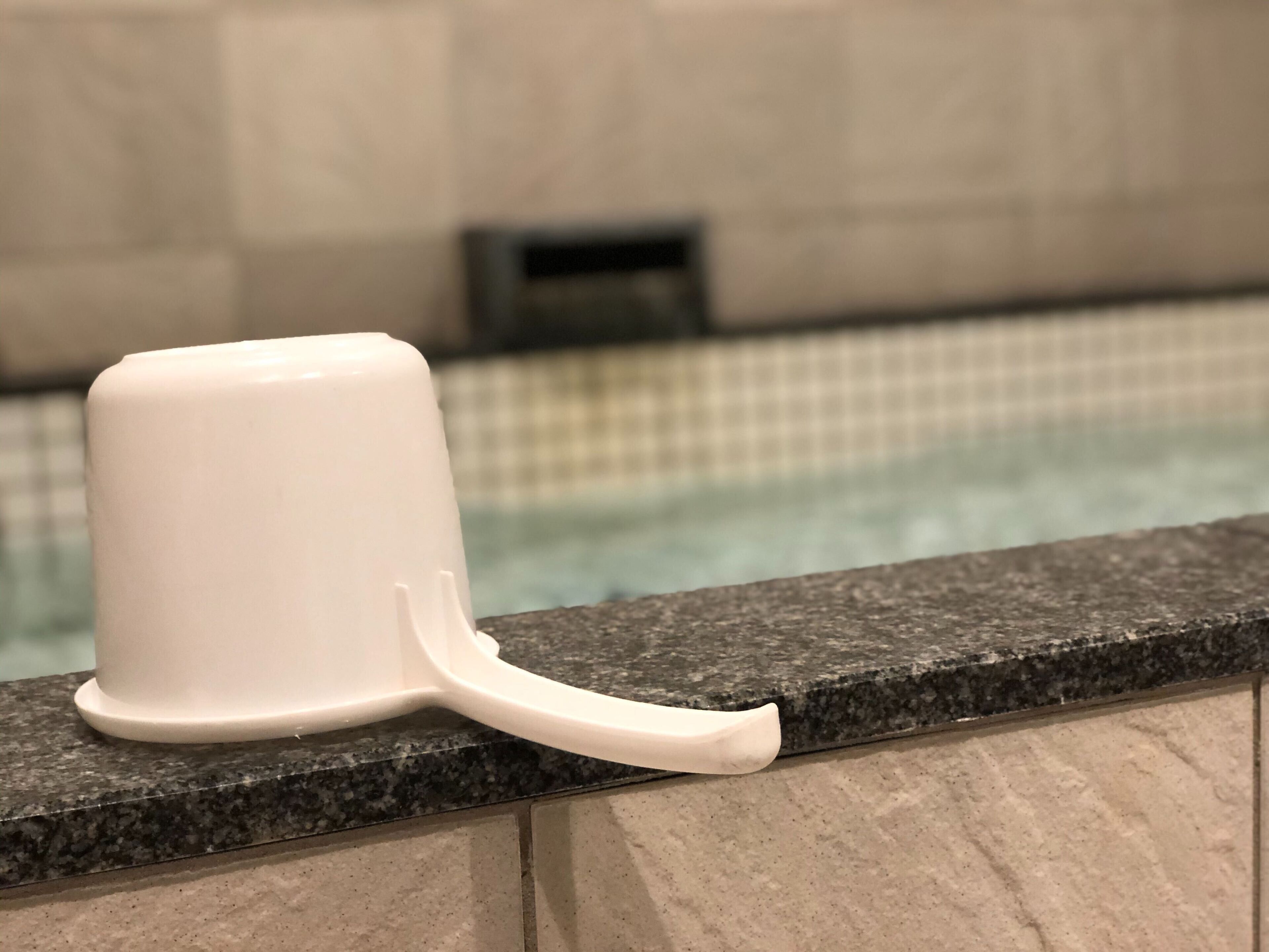 A white plastic cup on a granite countertop near a pool.