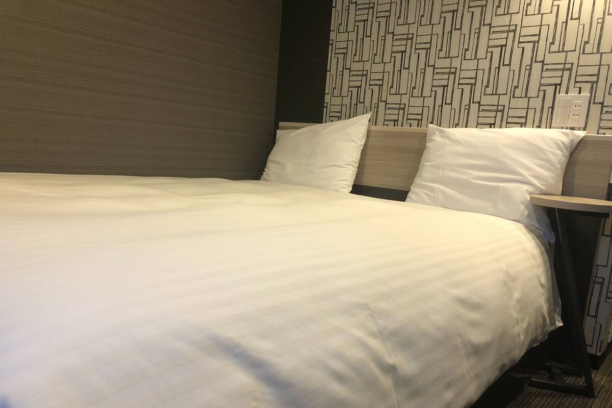 Una cama bien hecha con sábanas blancas, un cabecero con diseño geométrico y una mesita de noche con una lámpara.
