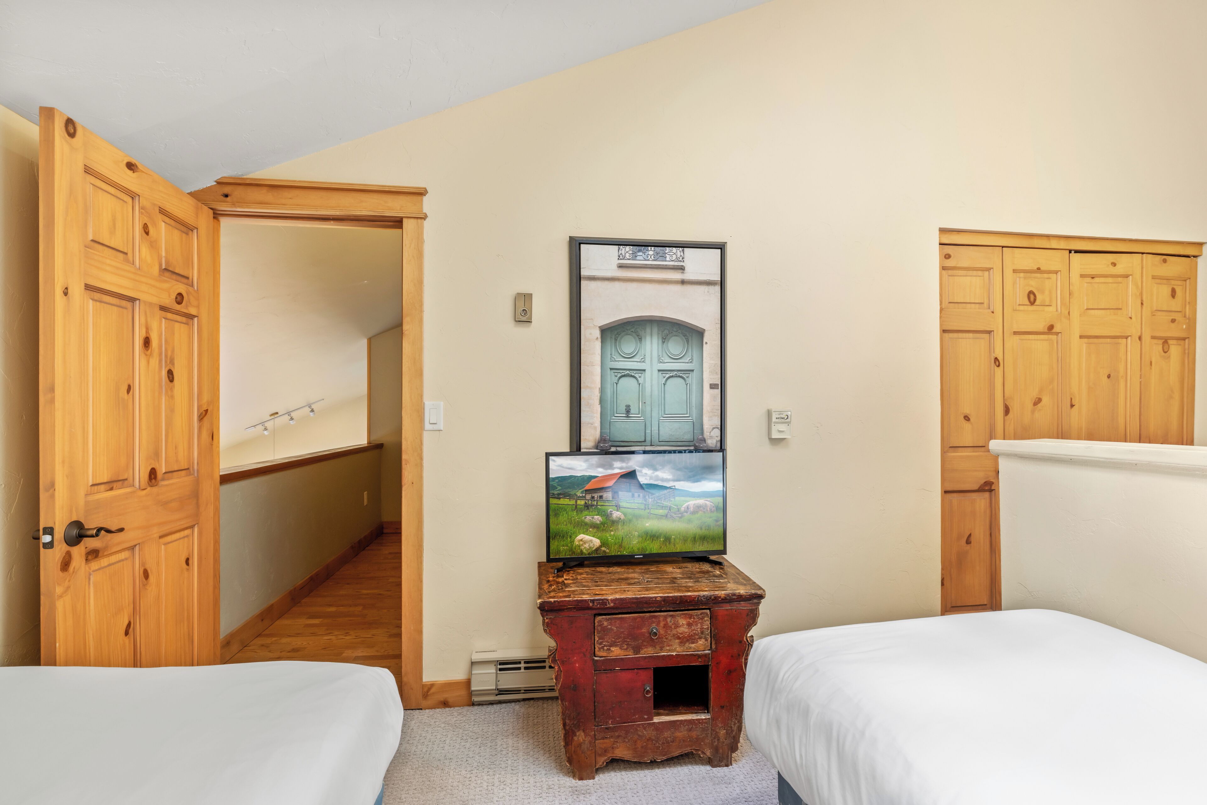A bedroom with two beds, wooden wardrobes, a small wooden dresser, and a painting on the wall.