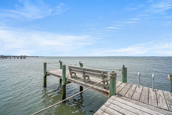 A wooden pier extending into calm water with a bench and metal railings.