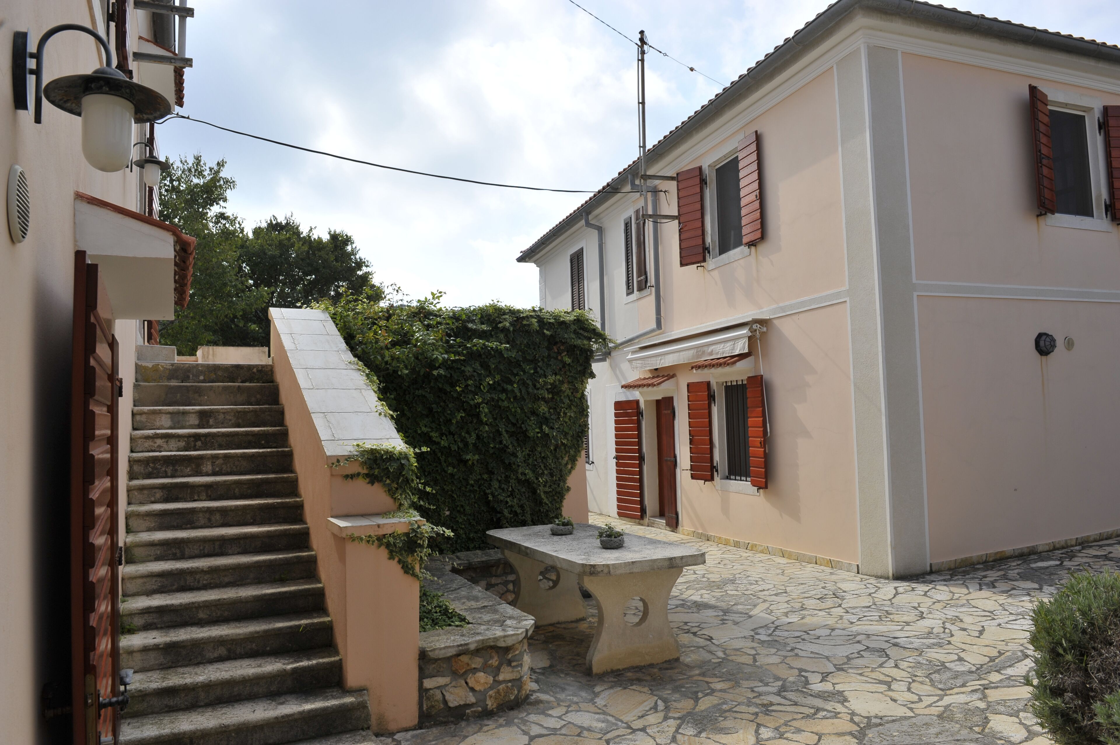 Un escalier en pierre mène à un bâtiment qui possède une table et des bancs en pierre dans sa cour.