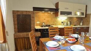 A kitchen with a stove, sink, and cabinets. There is a dining table set with plates, glasses, and a bowl of tomatoes.