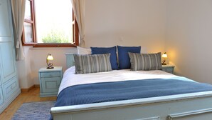 A bedroom with a bed, two bedside tables with lamps, a window with curtains, and a wooden floor.
