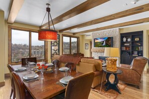 A dining area with a wooden table set for four, a fireplace, and a city view through large windows.