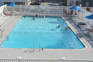 A rectangular swimming pool with a white deck, surrounded by white fences and blue umbrellas. - Colorful, spacious 2 bedroom oceanfront condo with WiFi, an outdoor pool, and a great ocean view located midtown and just steps to the beach! (Ocean City)