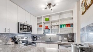 Une cuisine moderne dotée de plans de travail en granit, d’armoires blanches et d’un four encastré.