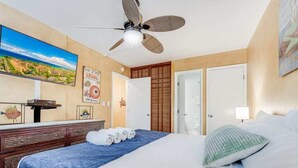 Une chambre d’hôtel équipée d’un lit, d’un ventilateur de plafond, d’une télévision et d’un mur donnant sur un paysage pittoresque.