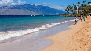 Una playa con agua azul cristalina, una montaña al fondo y algunas personas caminando por la orilla.
