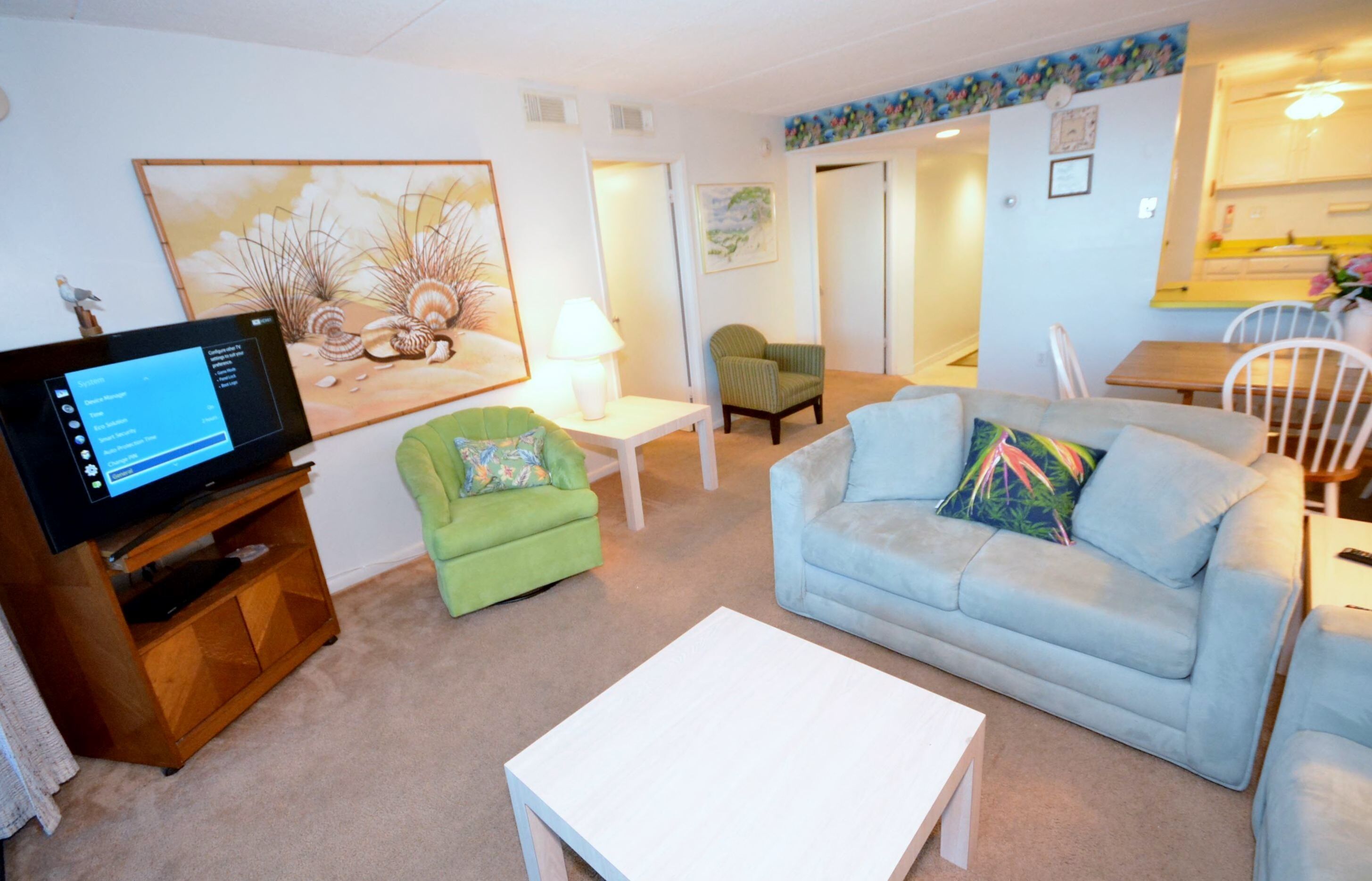 A living room with a television, a green armchair, a light blue sofa, and a white coffee table.