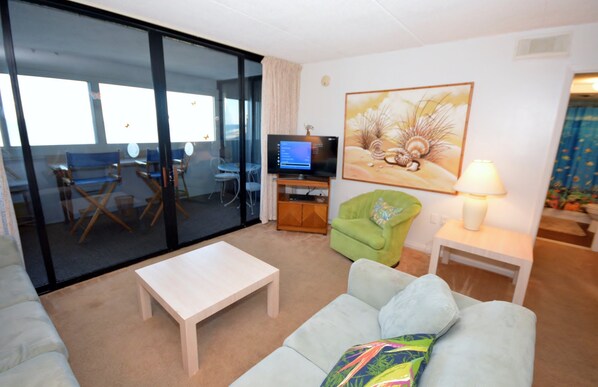 A living room with a sofa, a coffee table, a TV, a green armchair, and a painting on the wall.