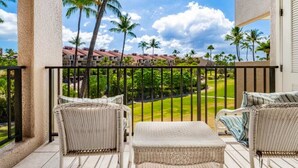 A balcony with wicker furniture and a view of a golf course and buildings. - Roomy West Maui Suite w/Cool Tile Floors, WiFi, Full Kitchen–Kamaole Sands 3205 (KIHEI)