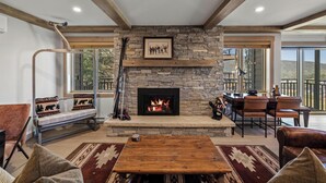 Una sala de estar acogedora con chimenea de piedra, un banco de madera, un comedor con sillas y un ventanal con vistas al exterior.