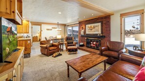 A spacious living room with a fireplace, leather furniture, and a kitchen area in the background. - Bear Claw 103 Mountain Condo With Ski-In/Ski-Out Access! (Steamboat Springs)