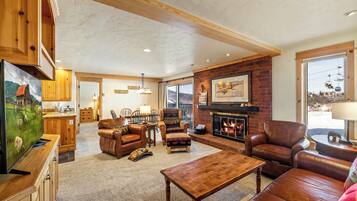 A spacious living room with a fireplace, leather furniture, and a kitchen area in the background.