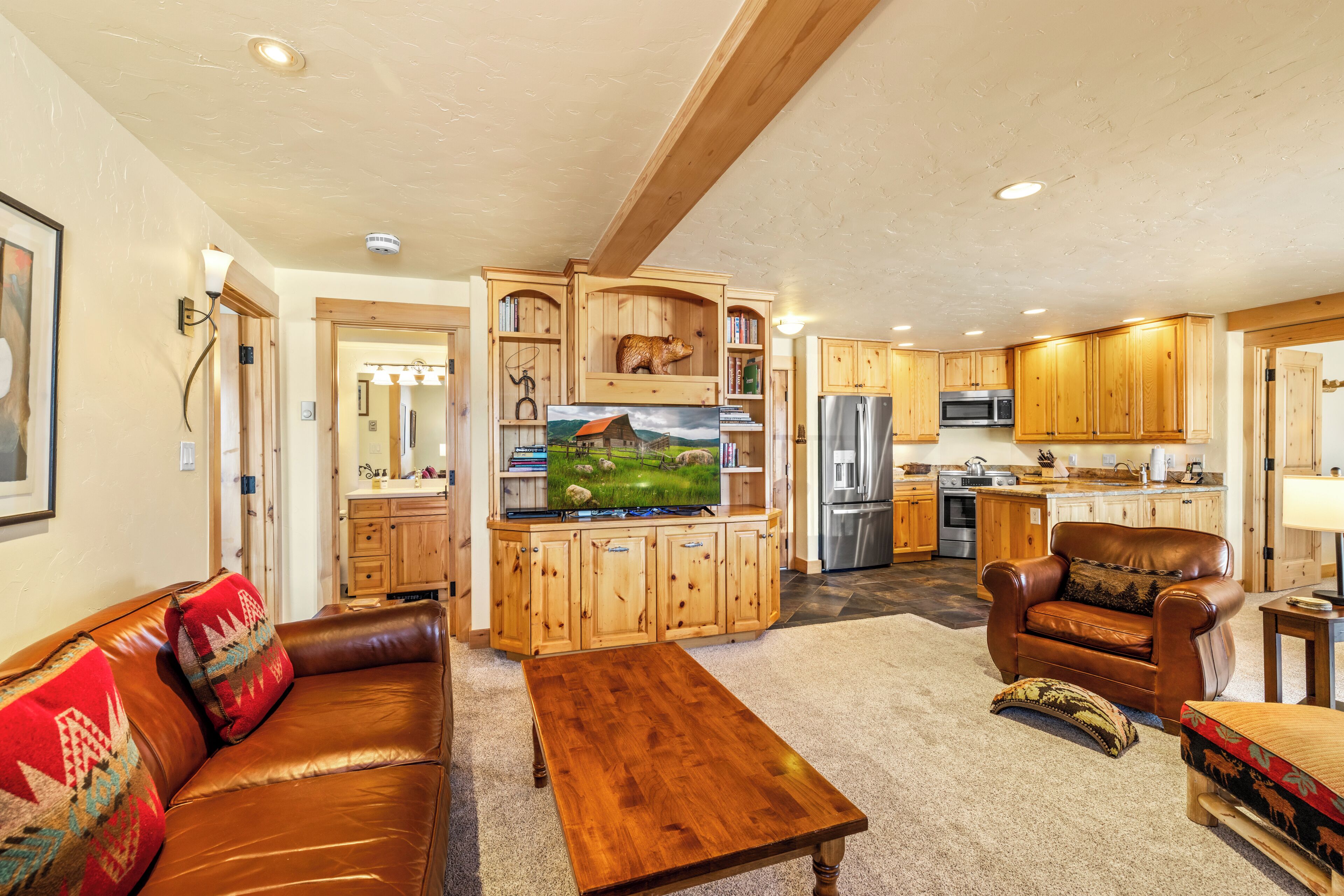 A spacious living room with a brown leather sofa, wooden entertainment center, and a dining table.