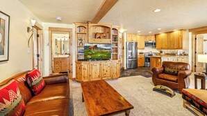 A spacious living room with a brown leather sofa, wooden entertainment center, and a dining table. - Bear Claw 103 Mountain Condo With Ski-In/Ski-Out Access! (Steamboat Springs)
