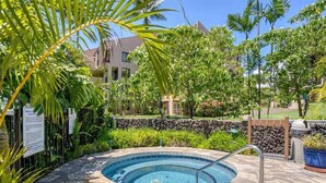 A circular hot tub surrounded by stone tiles, with a stone wall and greenery in the background. - Tranquil Courtyard View Condo w/Kitchen Updates, WiFi, Washer/Dryer–#7203 (KIHEI)