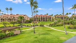 A hotel with multiple buildings, a well-maintained lawn, and palm trees. - Tranquil Courtyard View Condo w/Kitchen Updates, WiFi, Washer/Dryer–#7203 (KIHEI)