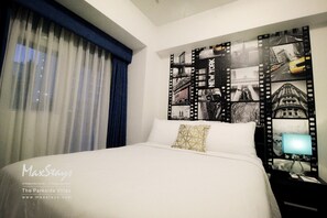 Habitación de hotel con una cama grande, una mesita de noche con lámpara y una pared decorada con fotografías tipo fotograma de película.