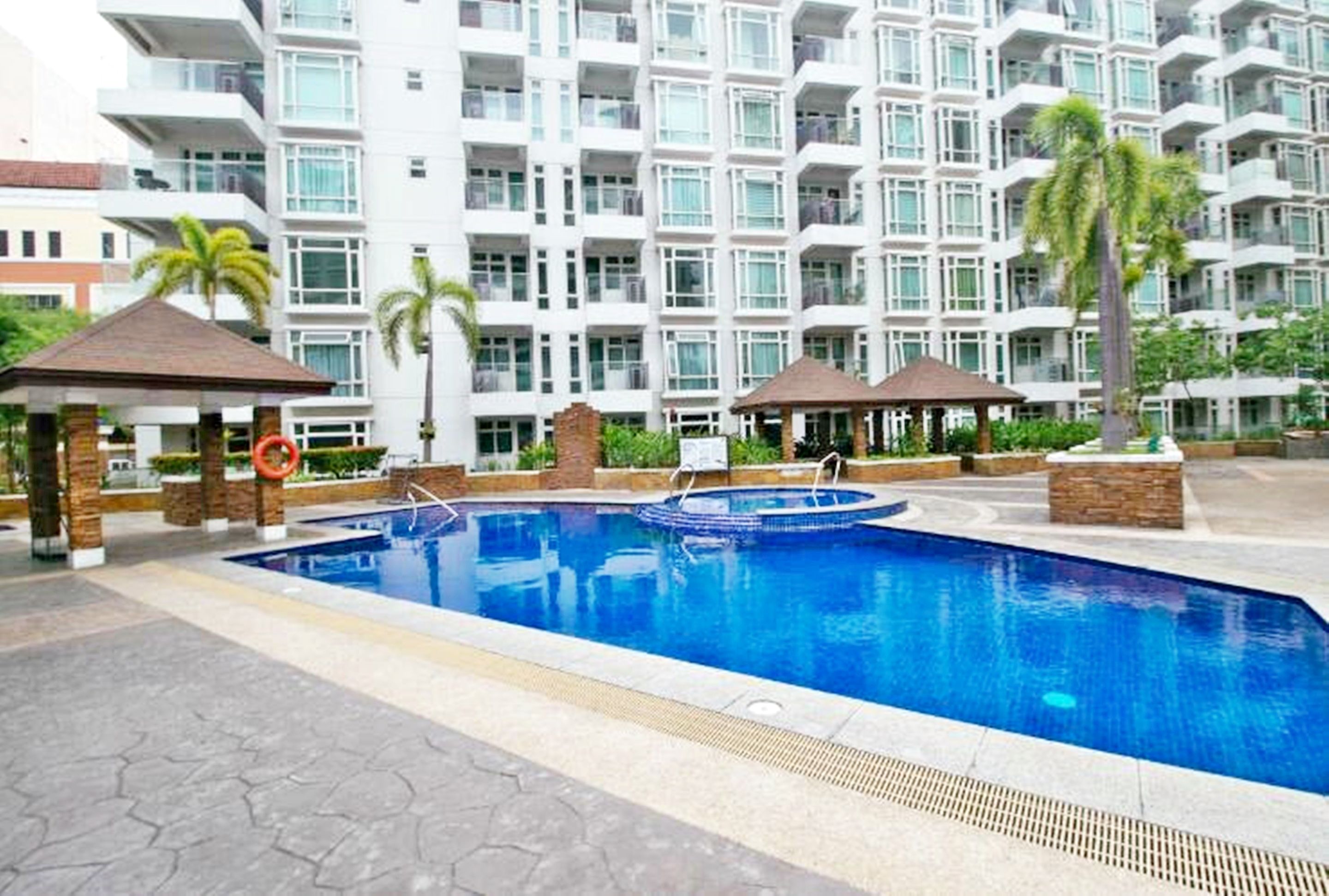 A swimming pool with lounge chairs and a gazebo, surrounded by a multi-story residential building with balconies.