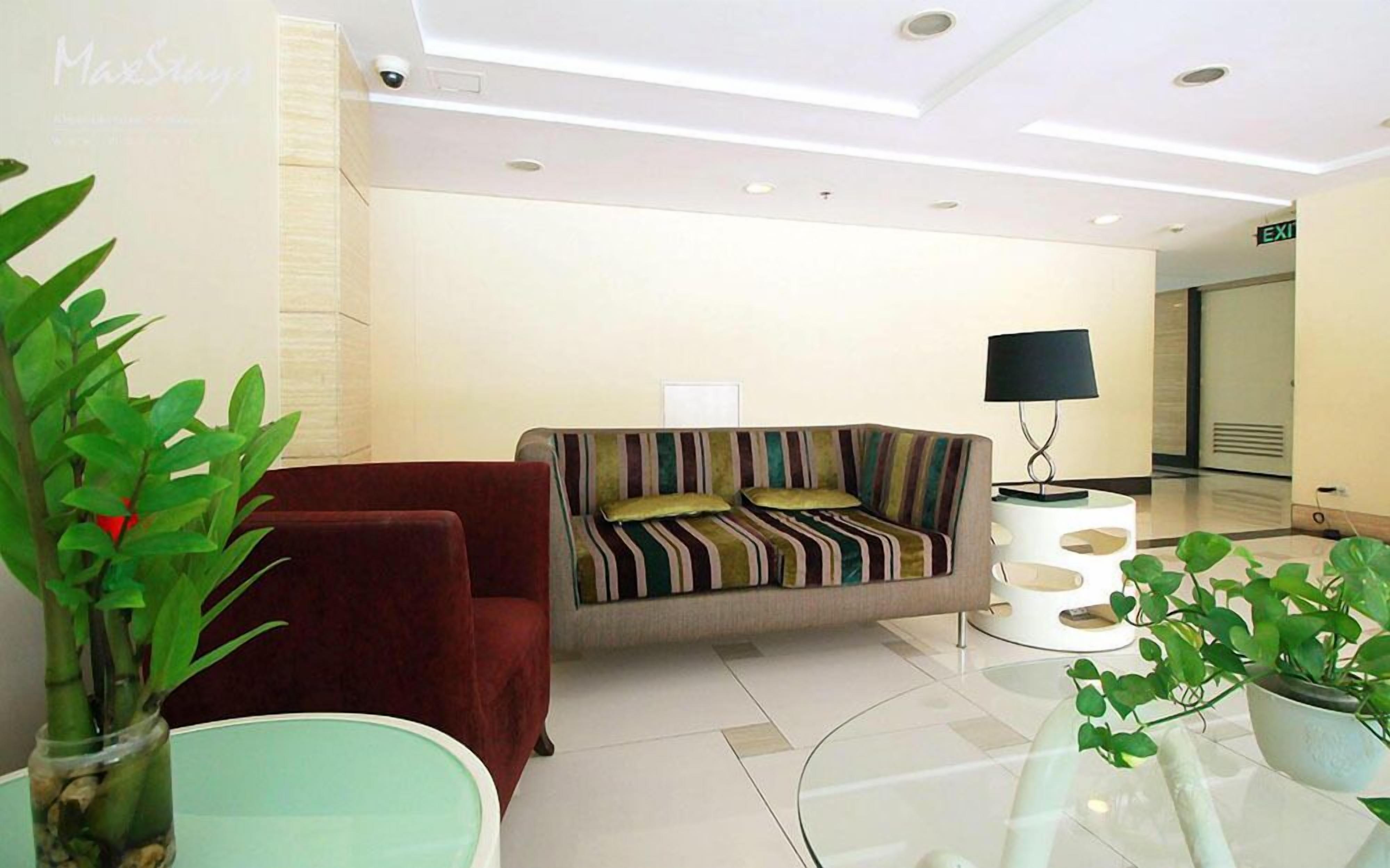 A modern hotel lobby with a sofa, a red chair, a glass table, and potted plants.