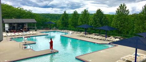 A swimming pool with lounge chairs and umbrellas, surrounded by trees.