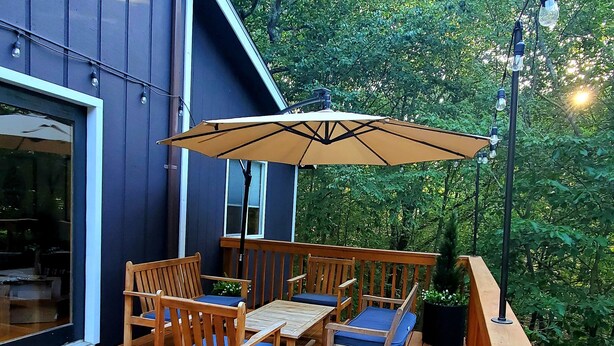 Eine Holzterrasse mit Tisch, Stühlen, einem großen Sonnenschirm und einem Blumentopf.