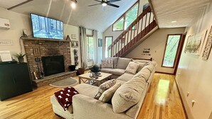 Ein geräumiges Wohnzimmer mit Kamin, einer großen Couch, einem Fernseher und einer Treppe zu einer oberen Ebene.