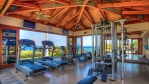 Et fitnesscenter med løbebånd, crosstrainere og styrkeudstyr, med udsigt over et smukt landskab.