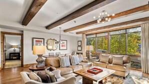 Ein geräumiges Wohnzimmer mit hoher Decke, Holzbalken, großen Fenstern und einer gemütlichen Sitzecke mit Sofas und einem Couchtisch.