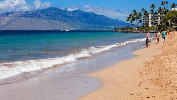 A beach with clear blue water, a mountain in the background, and a few people walking along the shore. - Island Energy in Suite w/Lanai, Washer/Dryer, WiFi, Kitchen–Kamaole Sands 7302 (KIHEI)