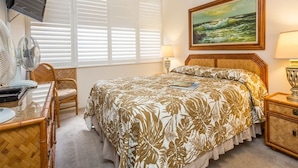 A bedroom with a bed, a television, a fan, a chair, and a painting on the wall. - Island Energy in Suite w/Lanai, Washer/Dryer, WiFi, Kitchen–Kamaole Sands 7302 (KIHEI)