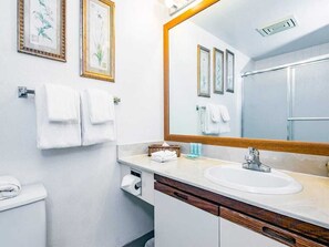 Une salle de bain avec un lavabo blanc, un meuble en bois et un grand miroir. Des serviettes sont accrochées au mur, et un panier contient une autre serviette.