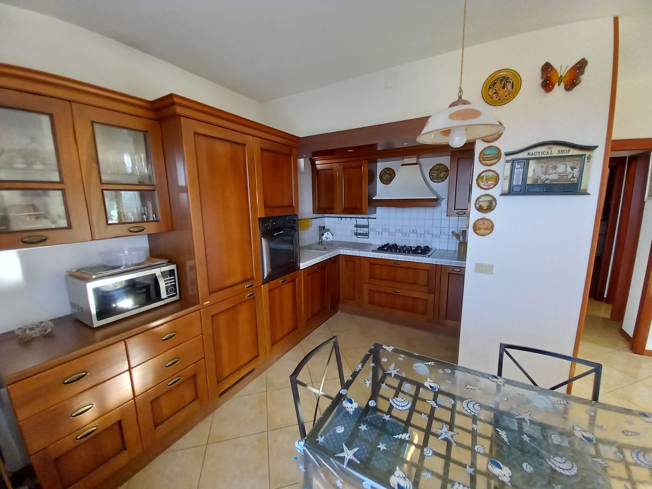 Una cucina compatta con mobili in legno, un forno a microonde, un fornello a gas e un tavolo da pranzo in vetro con motivo a stella.