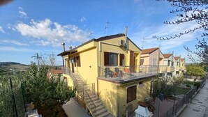 Une maison jaune à deux étages, dotée d’un balcon, d’un escalier et d’un jardin.